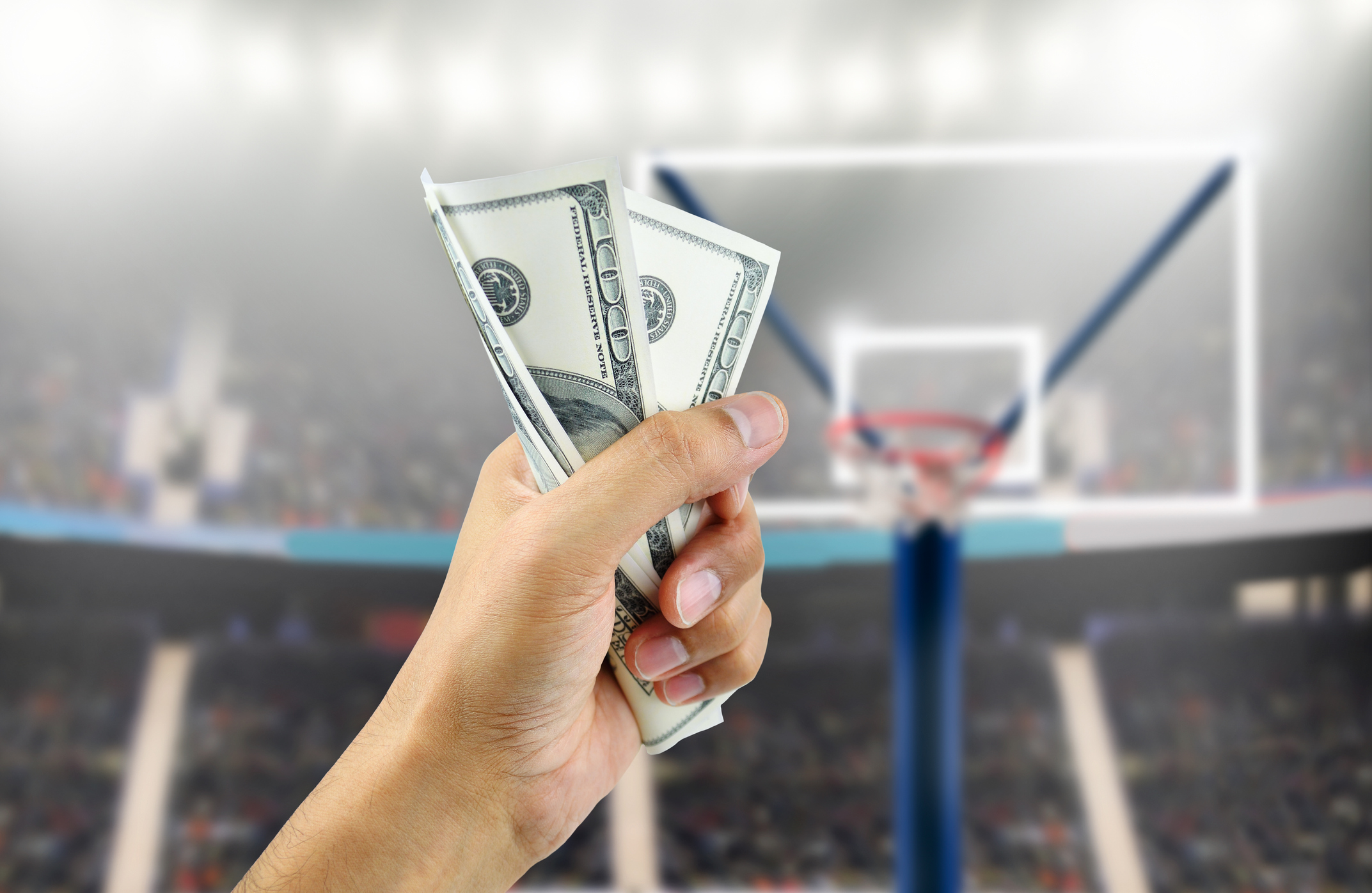 man's hand crushing a wad of hundred dollar bills in concept of getting money with bets in basketball
