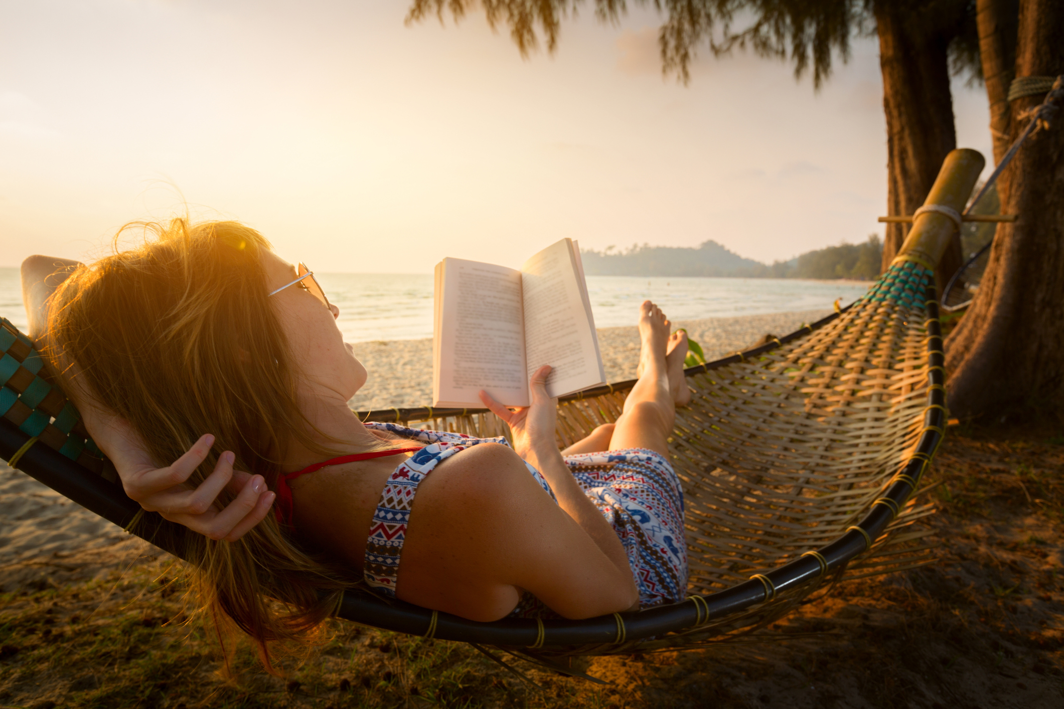 lady reading a book in hammock on a beach at sunset