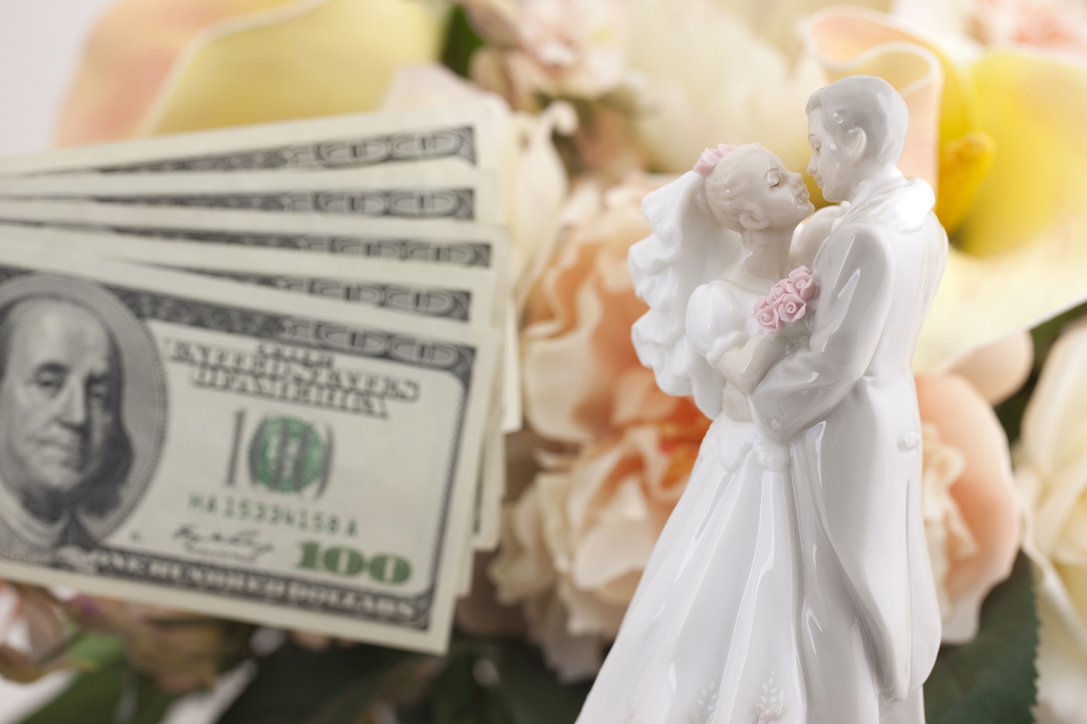 A wedding cake topper showing a groom and bride with one hundred dollars