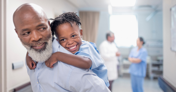 Older man in hospital with granddaughter on his back