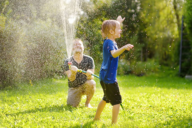Father spraying son with hose in summer heat